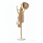 A gold metal coat rack with multiple curved hooks, displayed on a white background. It is styled with a beige wide-brim hat, a beige coat, a light pink scarf, and a small beige shoulder bag.