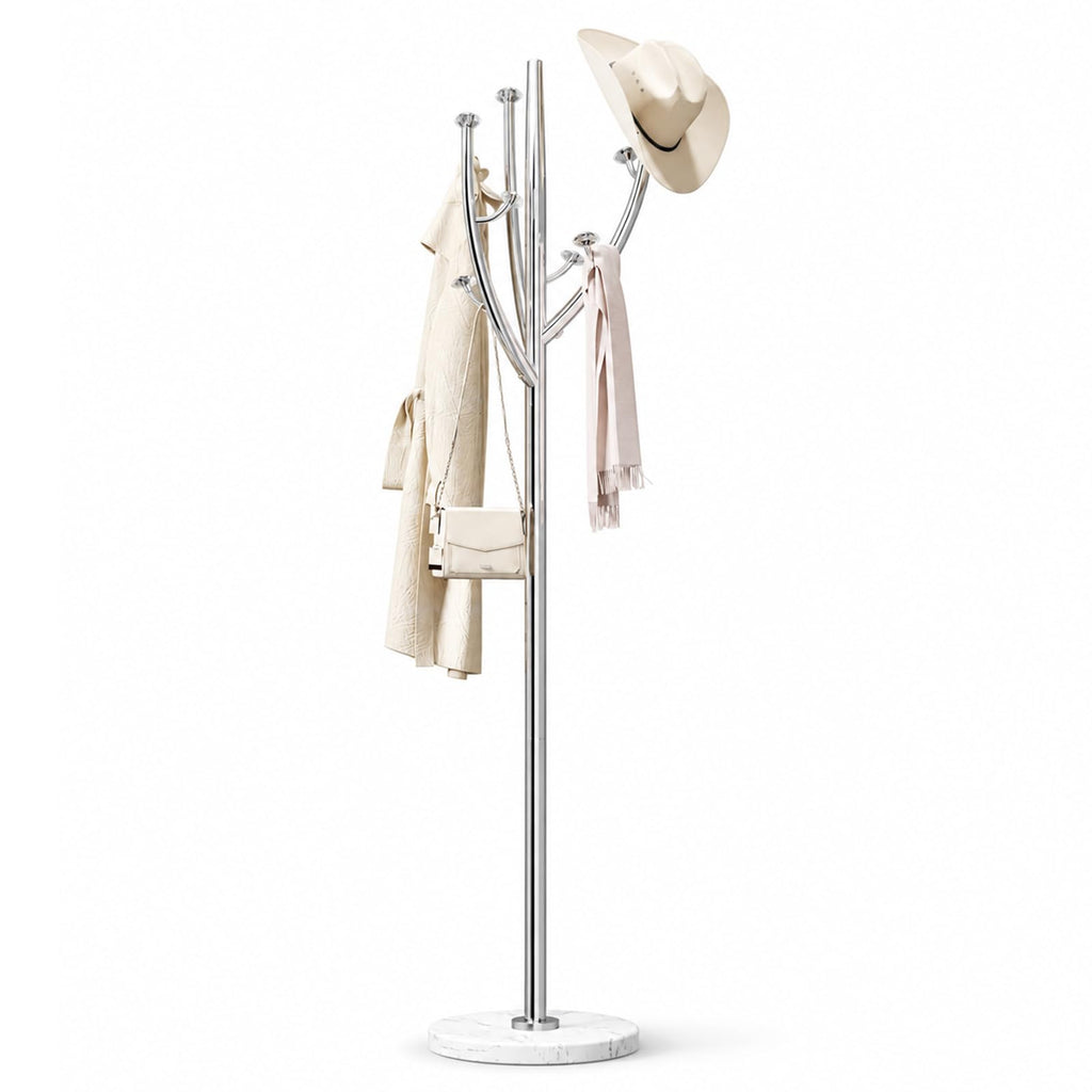 A modern silver coat rack with a round white marble base, styled with a cream trench coat, a light pink scarf, and a beige wide-brim hat, set against a solid white background.
