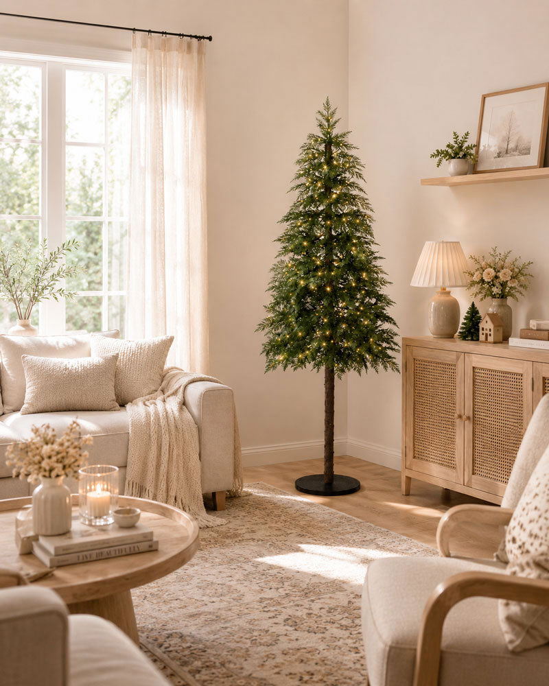 Cozy living room interior with a decorated Christmas tree, neutral-toned sofa, wooden cabinet, soft lighting, and natural sunlight. The warm minimalist space features seasonal decor, woven textures, and a comfortable home atmosphere.